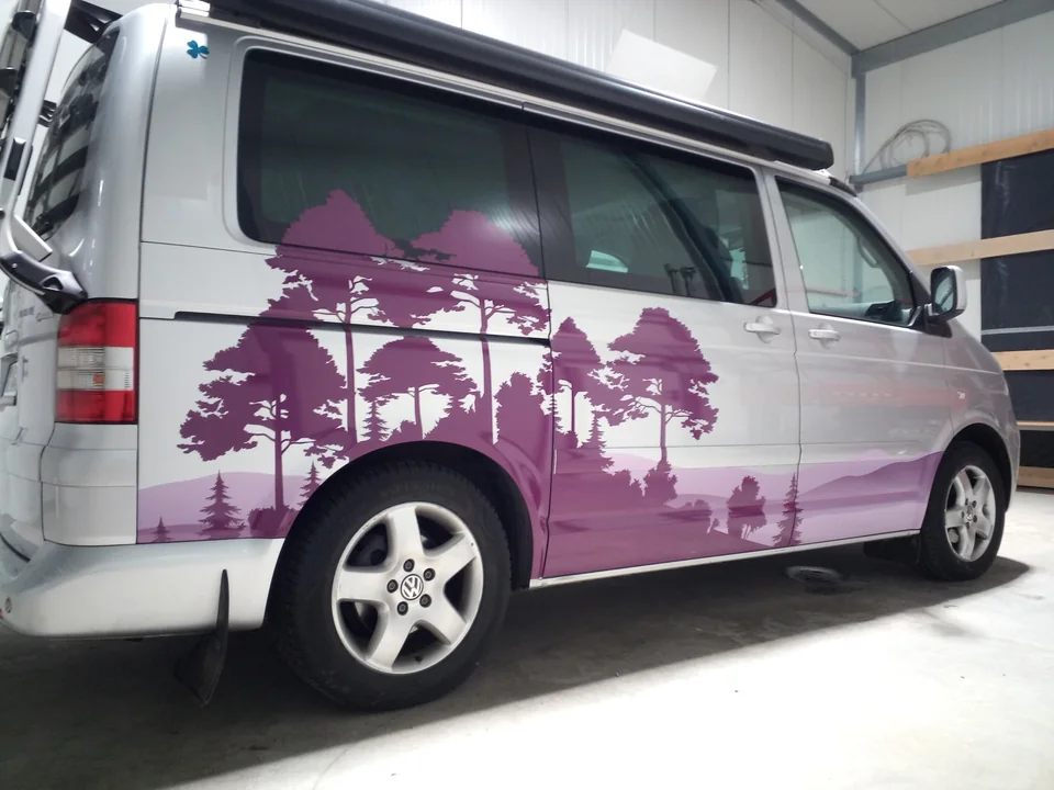 Silberner Camper mit violettem Wald- und Bergmotiv auf der Seite