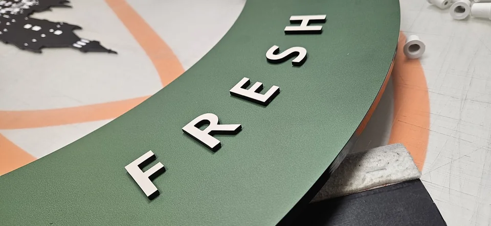 Weiße dreidimensionale Buchstaben auf einer grünen Trägerplatte