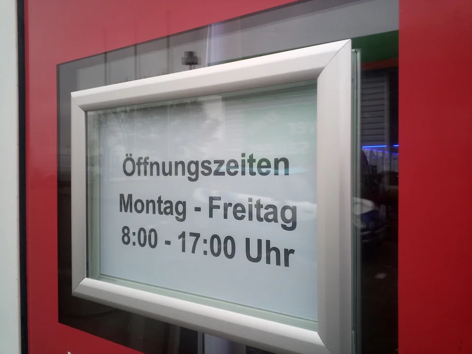 Gerahmtes Schild mit Öffnungszeiten an einer roten Eingangstür