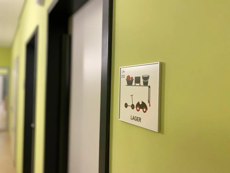 Lagerschild mit Raumnummer und Piktogrammen neben einer Tür