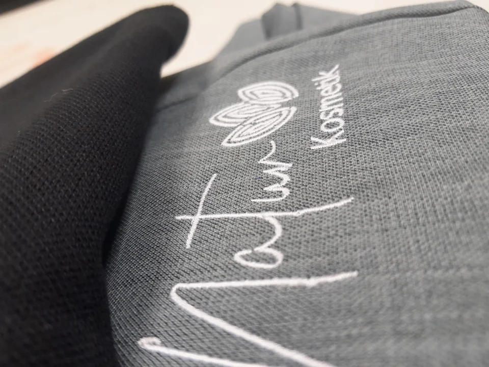 Nahaufnahme einer weißen Logostickerei auf grauem Textil